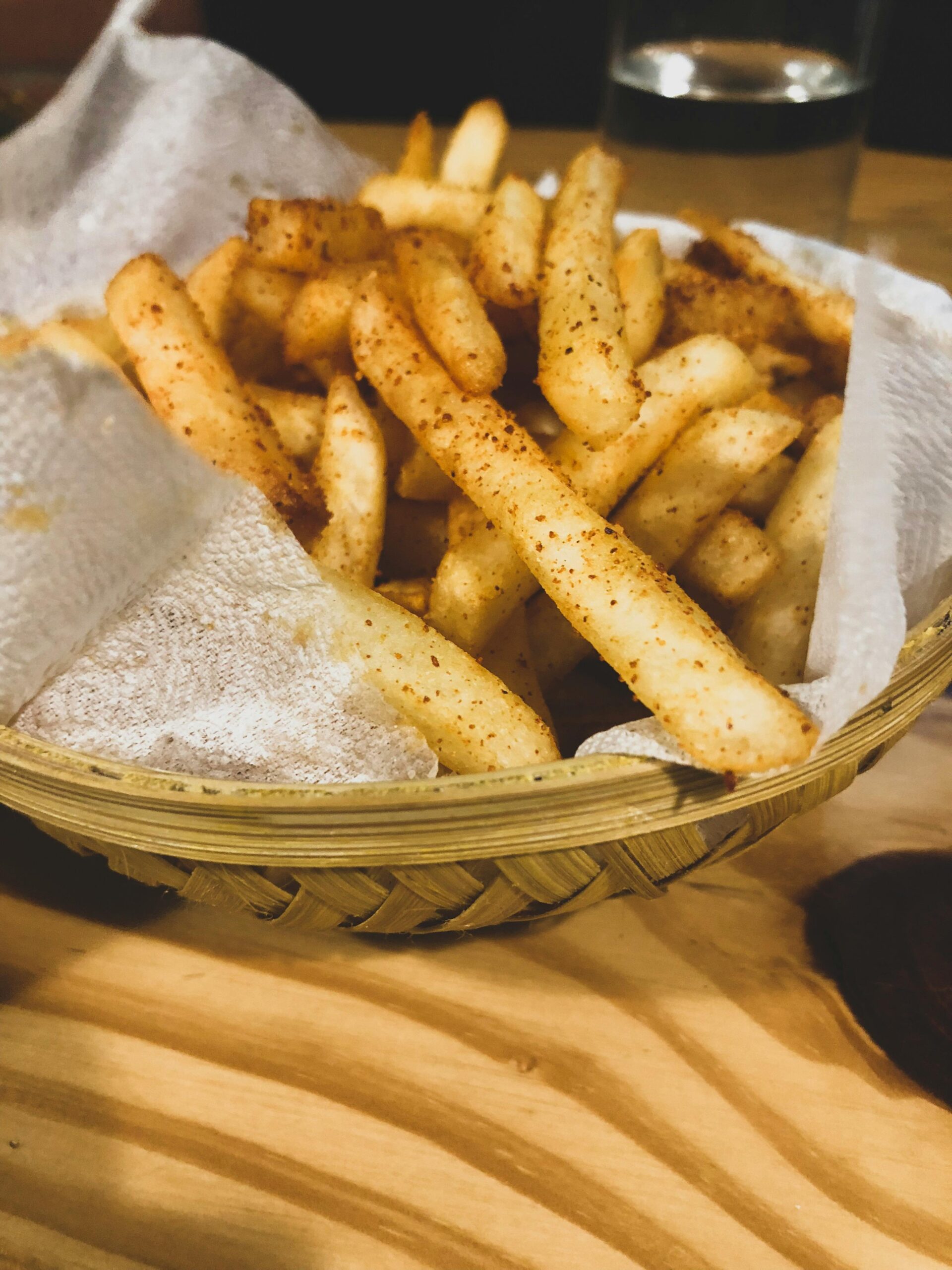 Close-up of seasoned french fries served in a rustic basket on a wooden table.